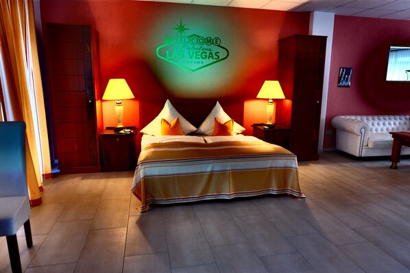 Una habitación de hotel con una cama, dos lámparas de noche, un letrero de neón que dice "Welcome Fabulous Las Vegas Nevada", un televisor en la pared y un sofá.