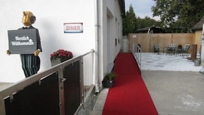 Ein Gebäudeeingang mit rotem Teppich, einem 'DINER'-Schild und einem 'Herzlich Willkommen'-Schild.