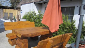 Ein Holztisch mit Bänken, ein roter Sonnenschirm und ein Schild mit der Aufschrift 'Boardinghouse'.