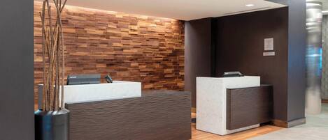 A reception area with a modern design, featuring a wooden wall, a reception desk, and a large vase with decorative branches.