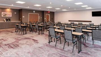A conference room with multiple tables and chairs, a reception desk, and a clock on the wall.