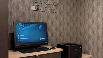A desk with a computer, a printer, and a wall sign that reads "Quick Print".