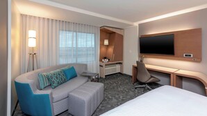 Una habitación de hotel moderna con sofá, escritorio, televisor y cama.