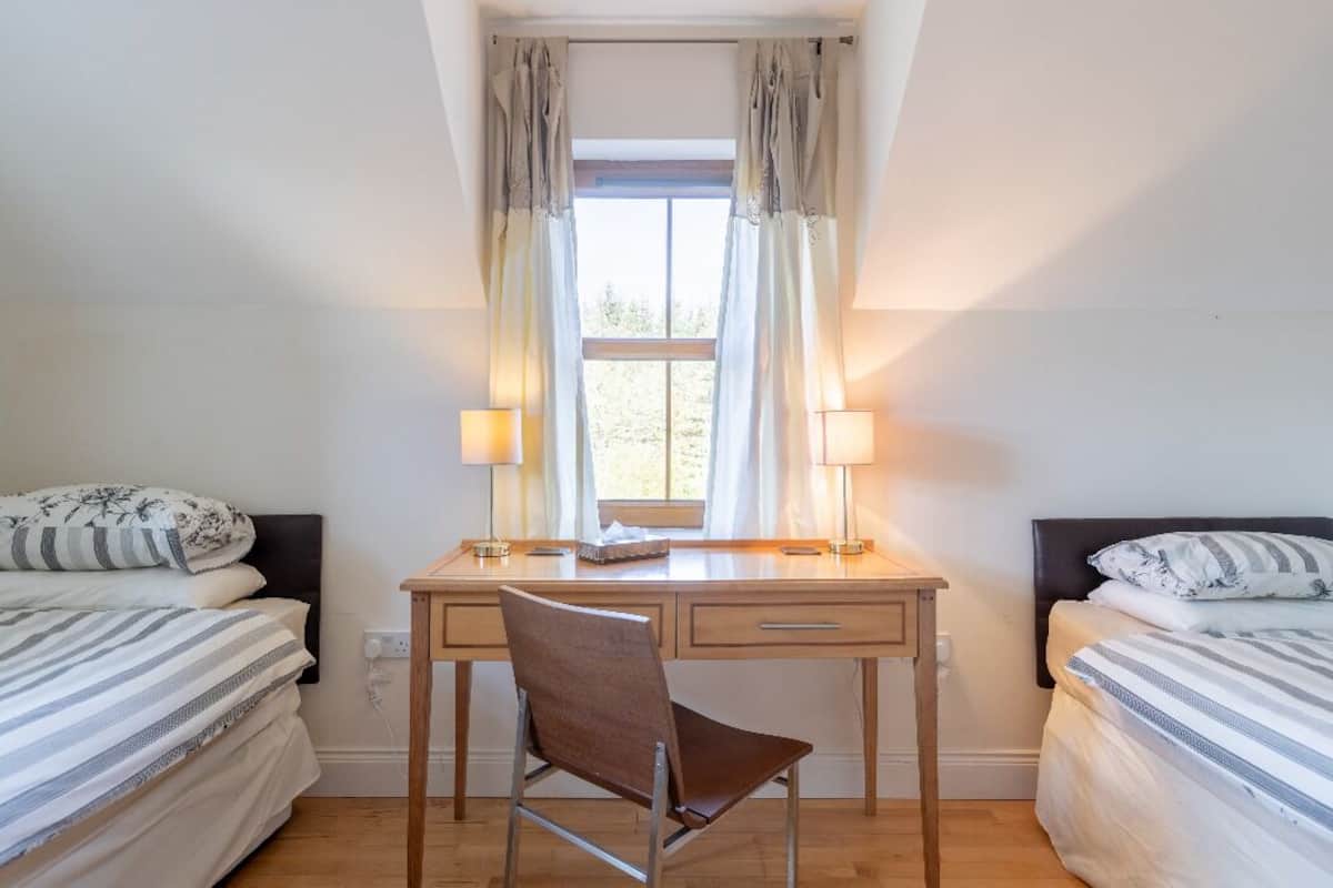 Un dormitorio con una cama individual, un escritorio con dos lámparas, una silla y una ventana con cortinas.