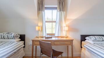 A bedroom with a single bed, a desk with two lamps, a chair, and a window with curtains.
