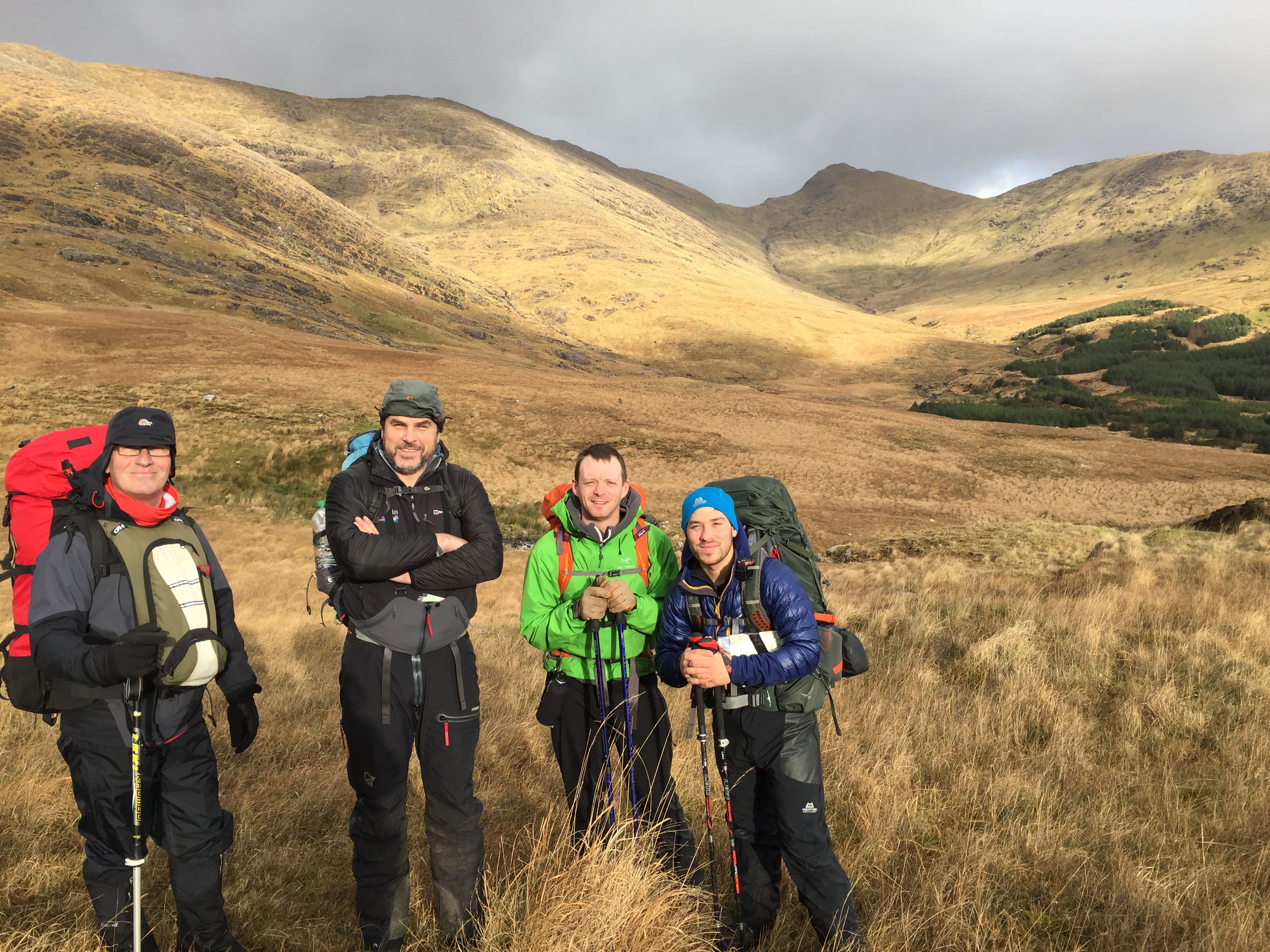 Three hikers in a mountainous area with dry grass and hills in the background.