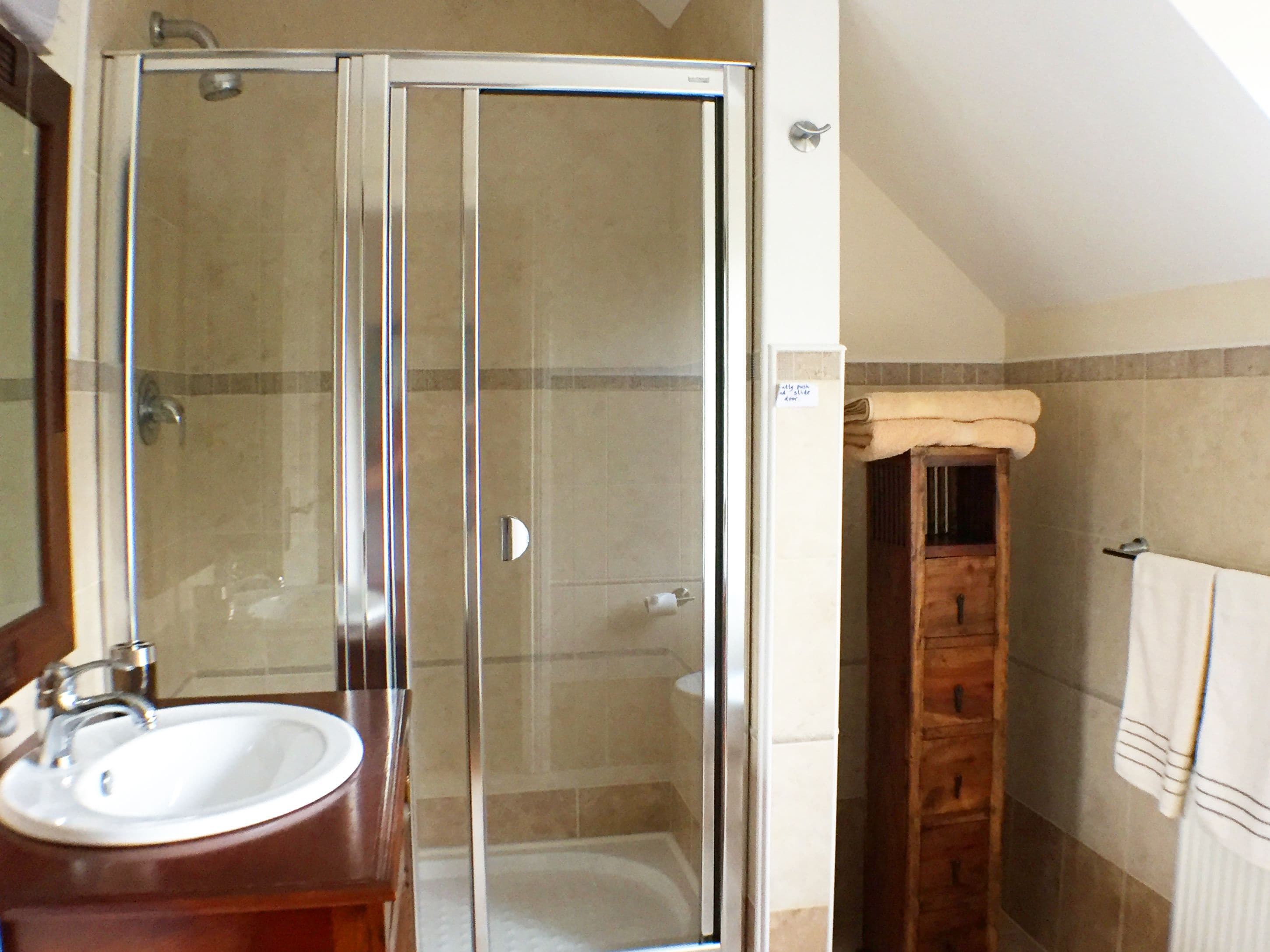A bathroom with a glass shower enclosure, a white sink, and a wooden cabinet.