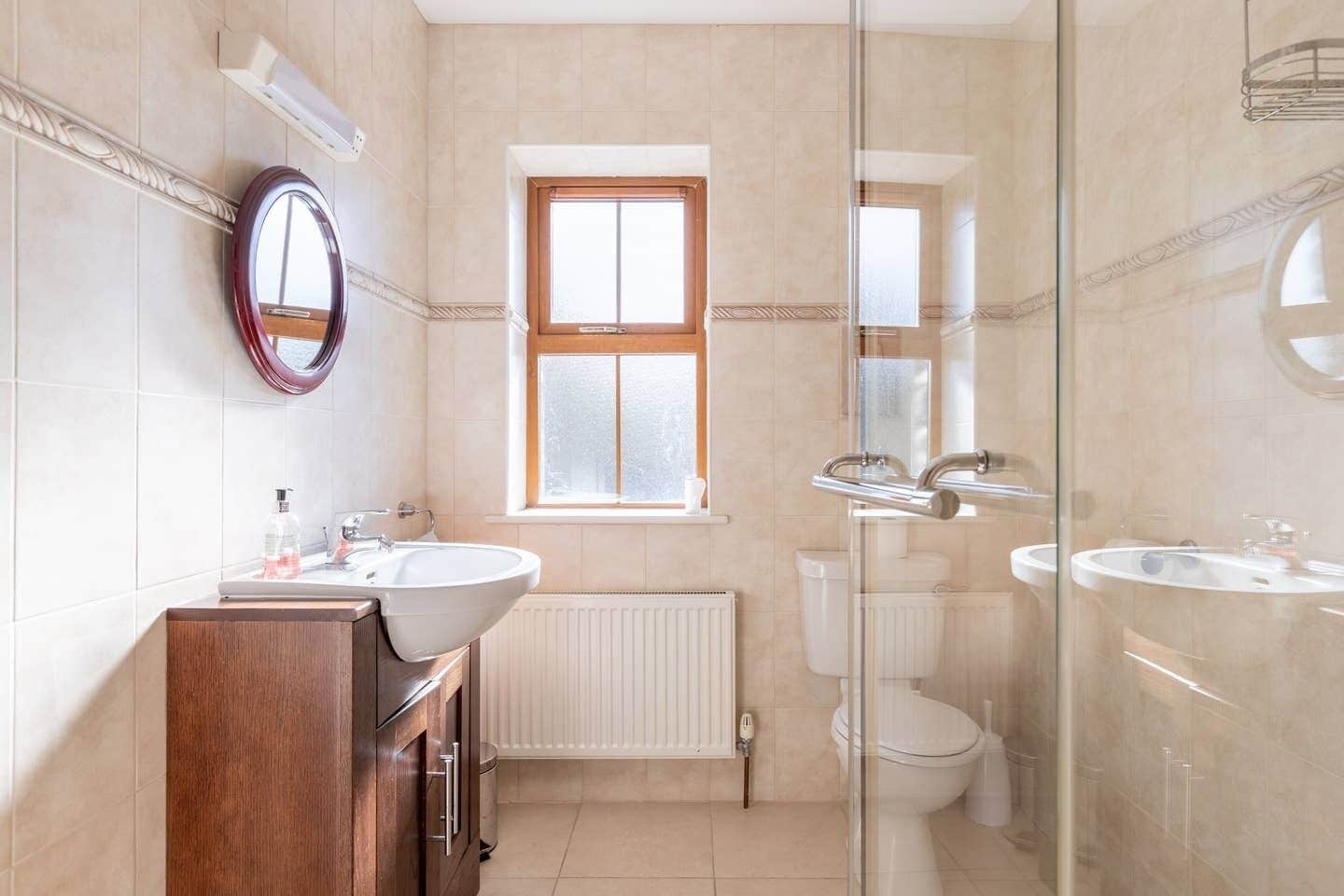 A modern bathroom with two sinks, a mirror, a window, and a glass shower enclosure.