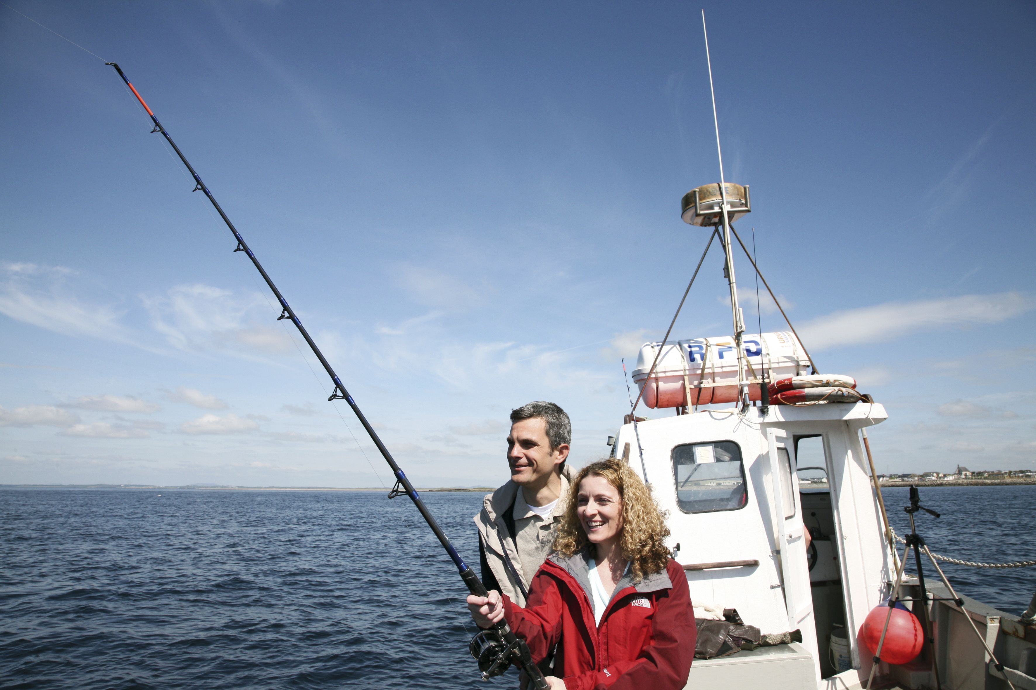 A boat on the water with two people holding fishing rods.