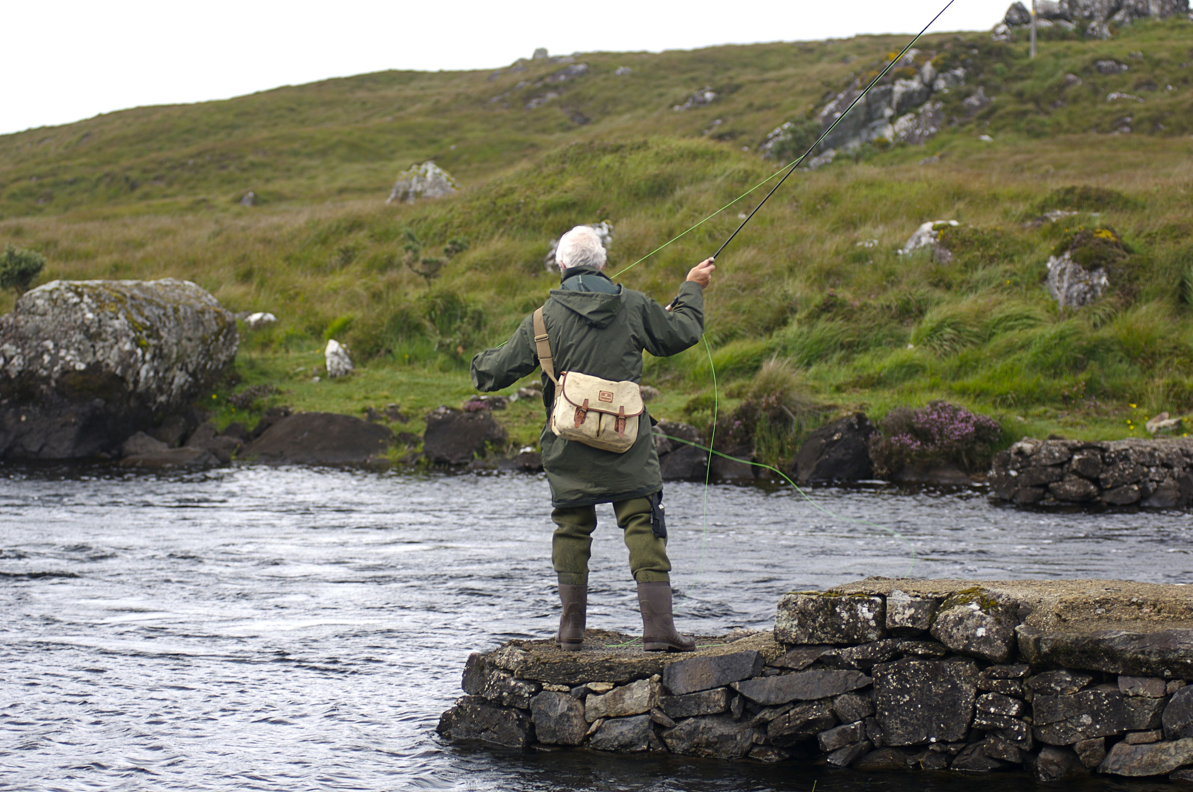 Una persona en una plataforma de piedra junto a un río, pescando con una caña.