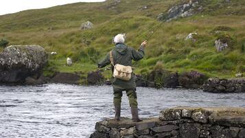 Una persona en una plataforma de piedra junto a un río, pescando con una caña.
