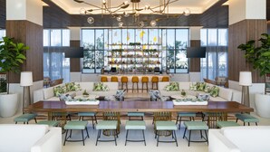 A spacious bar area with a long counter, multiple seating options, and a large window providing a view of the outdoors. - The Dalmar, Fort Lauderdale, a Tribute Portfolio Hotel (Fort Lauderdale)