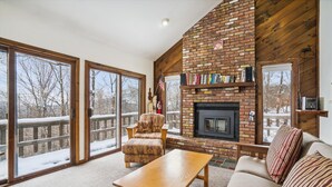 A cozy living room with a brick fireplace, a sofa, a wooden coffee table, and a bookshelf filled with books. - Three bedroom Private home with Beautiful Views & Short Walk to the Home Stretch Trail! Frosty (Killington)