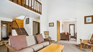 A spacious living room with a wooden staircase, a sofa with striped pillows, a wooden coffee table, and a chair. - Three bedroom Private home with Beautiful Views & Short Walk to the Home Stretch Trail! Frosty (Killington)