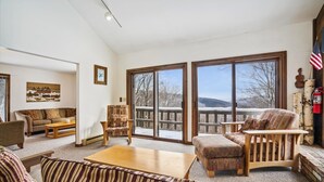 A spacious living room with a large window, a wooden deck, and a view of a snowy landscape. - Three bedroom Private home with Beautiful Views & Short Walk to the Home Stretch Trail! Frosty (Killington)