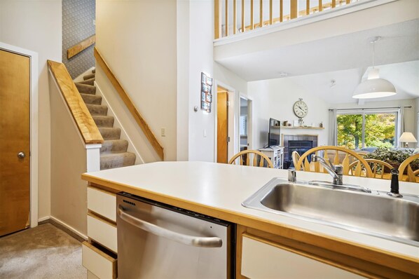 Una cocina moderna con lavavajillas, sillas de madera, una mesa de comedor y una escalera.