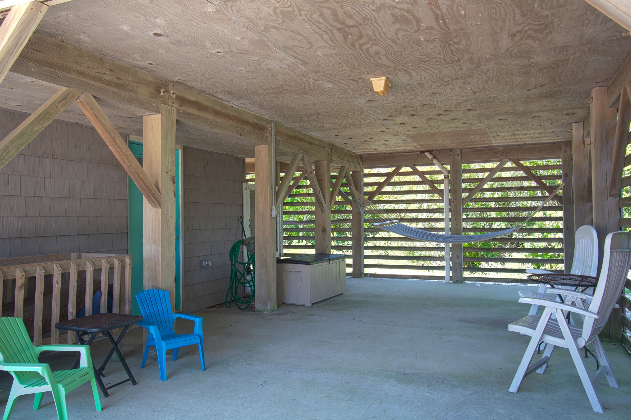 A covered outdoor seating area with wooden beams, a hammock, and two tables with chairs.