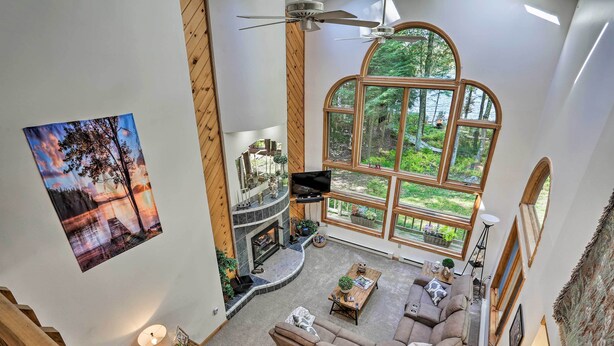 A spacious living area with a fireplace, large windows offering a forest view, and a cozy seating arrangement. - Pocono Lake Paradise w/ Private Beach & Dock! (Pocono Lake)