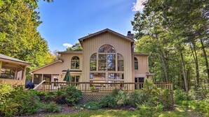A large, two-story house with a wrap-around porch, surrounded by lush greenery and trees. - Pocono Lake Paradise w/ Private Beach & Dock! (Pocono Lake)