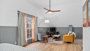 Una sala de estar moderna con sofá, sillón, televisor y ventilador de techo.