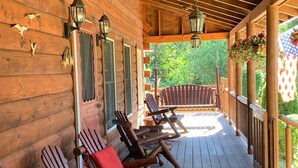 A wooden cabin with a porch featuring wooden chairs with red cushions, a wooden railing, and hanging lanterns. - Indulge in the ultimate vacation experience at this exquisite custom log home.  (Oak Bluffs)