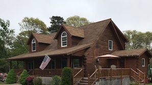 A wooden cabin with a porch, a covered deck, and a gravel driveway. - Indulge in the ultimate vacation experience at this exquisite custom log home.  (Oak Bluffs)