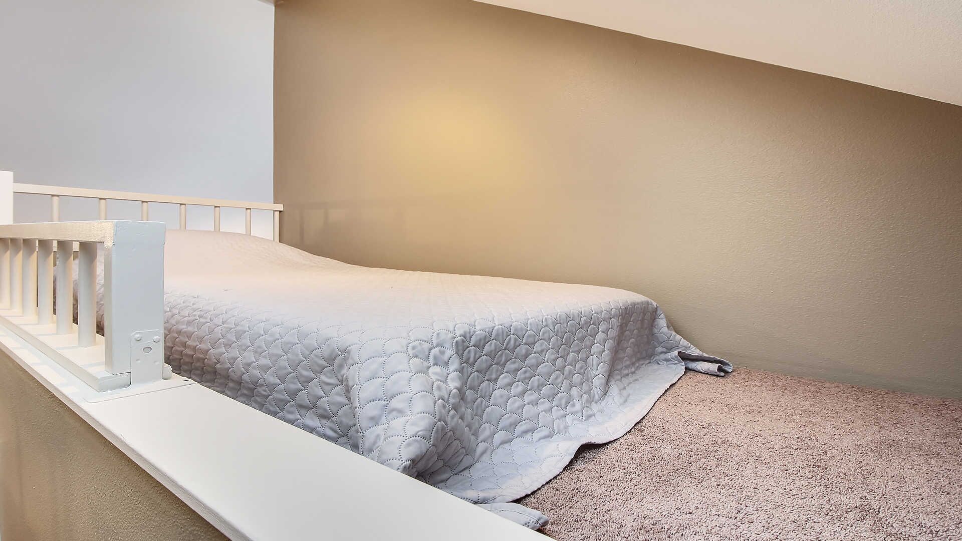 Ein kleines Zimmer mit einem Einzelbett, weißer Bettdecke, weißer Geländer und Teppichboden.