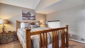 Un dormitorio con una cama de madera, dos mesitas de noche, una lámpara y un cuadro en la pared.