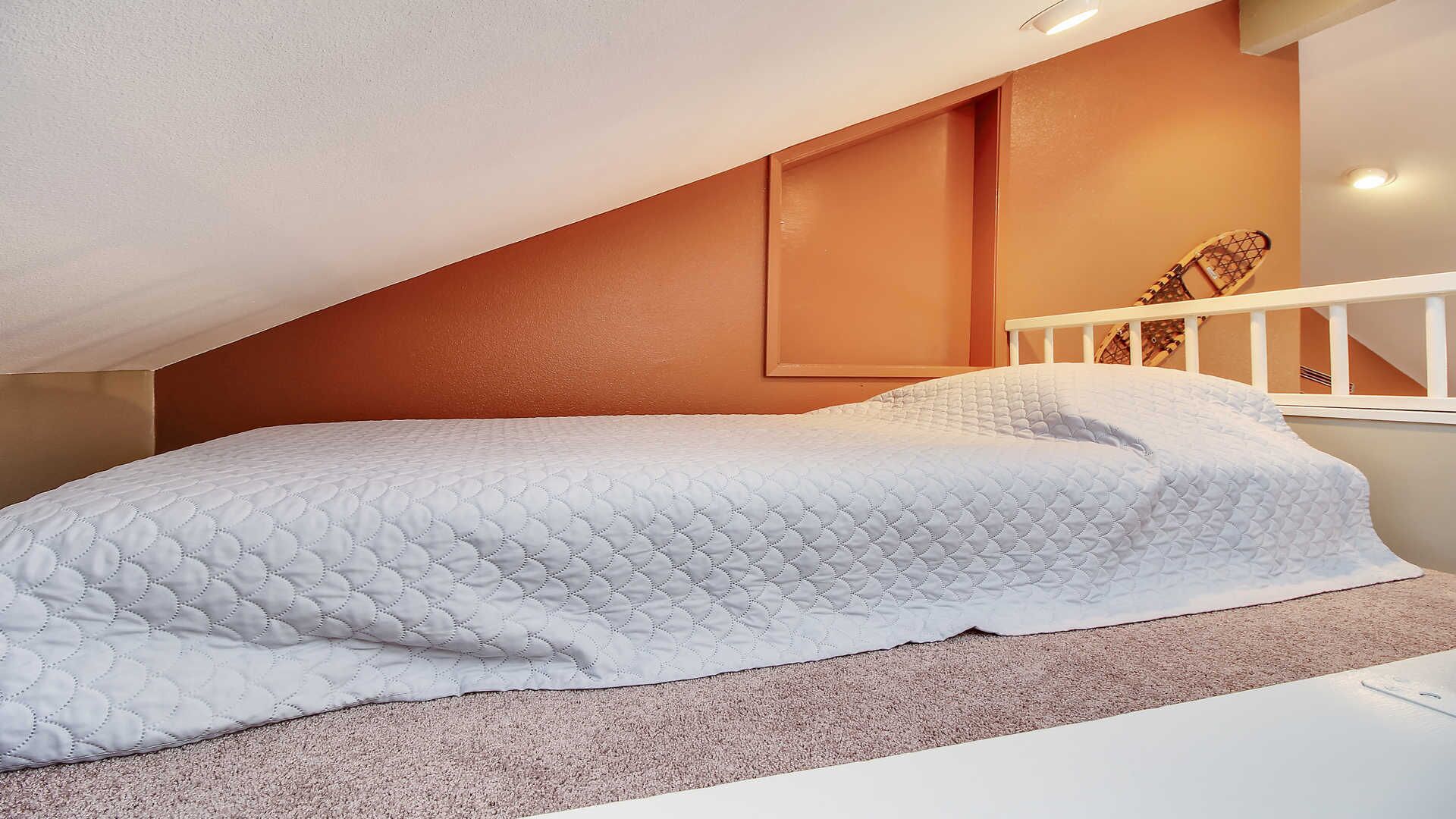 Une chambre avec un lit blanc, un plafond en pente et une tête de lit en bois.