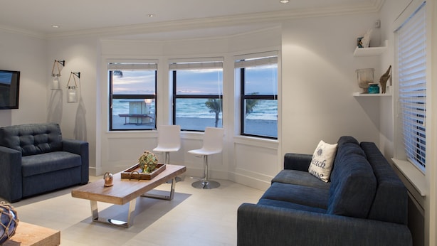A modern living room with a view of the ocean, featuring a blue sofa, a wooden coffee table, and a white armchair. - Direct Ocean & Boardwalk Views - Beautifully Appointed Condo - Parking & Wi-Fi (Hollywood)