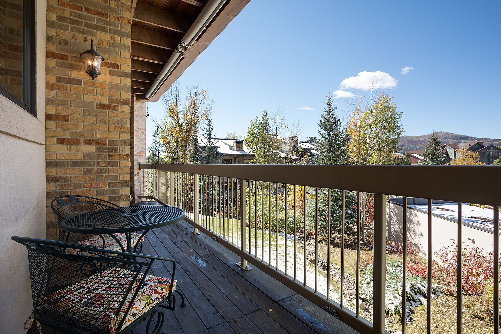 A wooden deck with metal chairs and a table, overlooking a residential area with trees and houses.