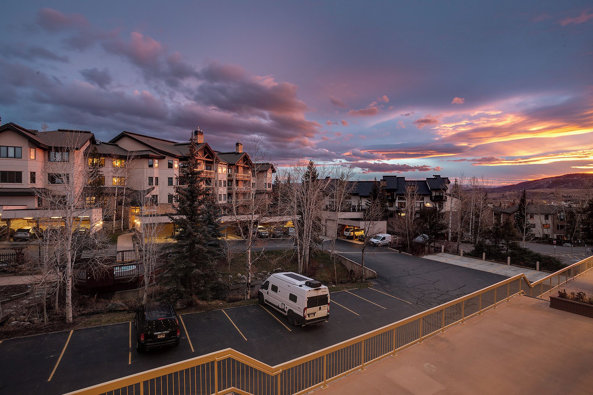 A residential area with multi-story buildings, a parking lot, and a van parked in the foreground.