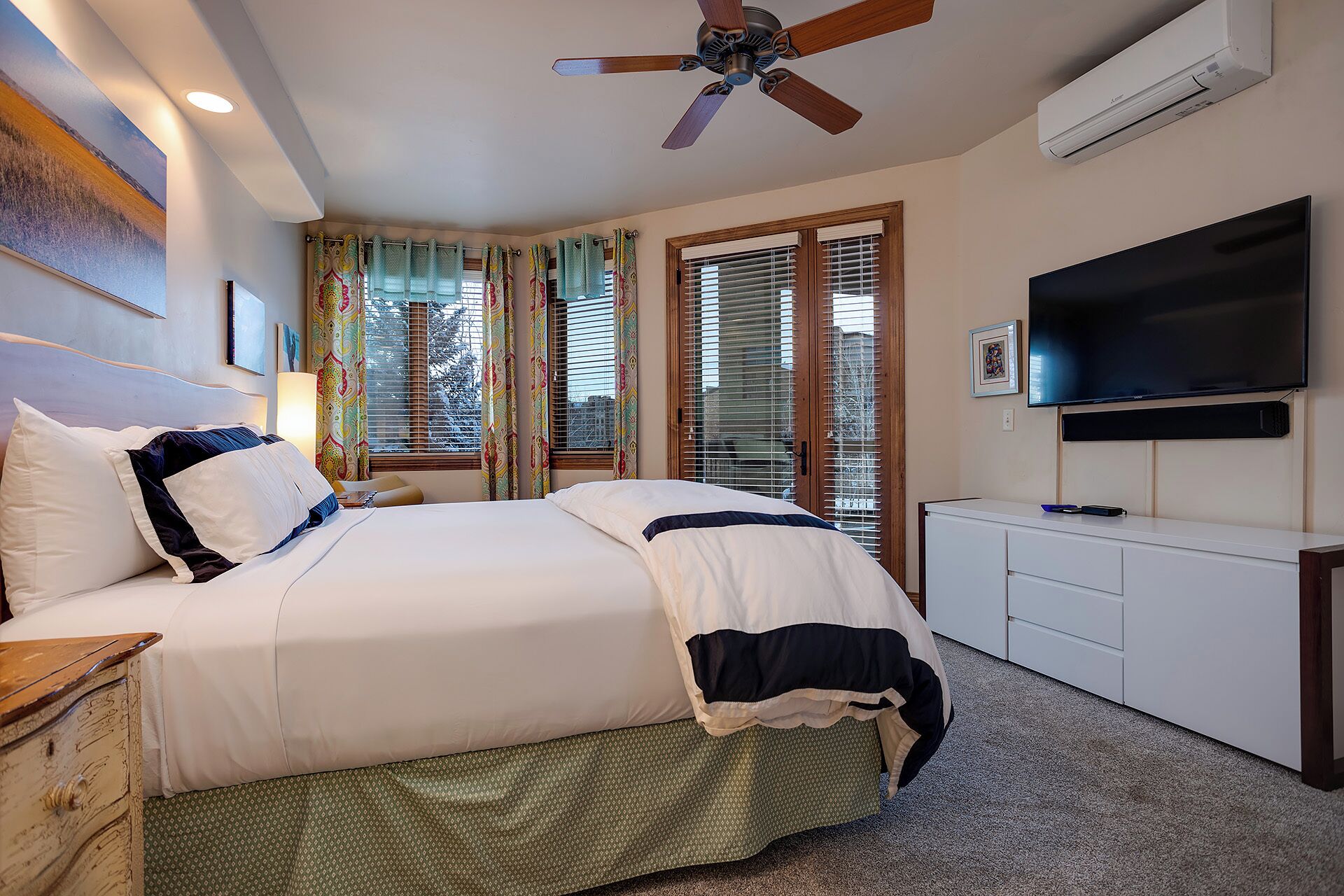A hotel room with a bed, a ceiling fan, a TV, and a window with curtains.