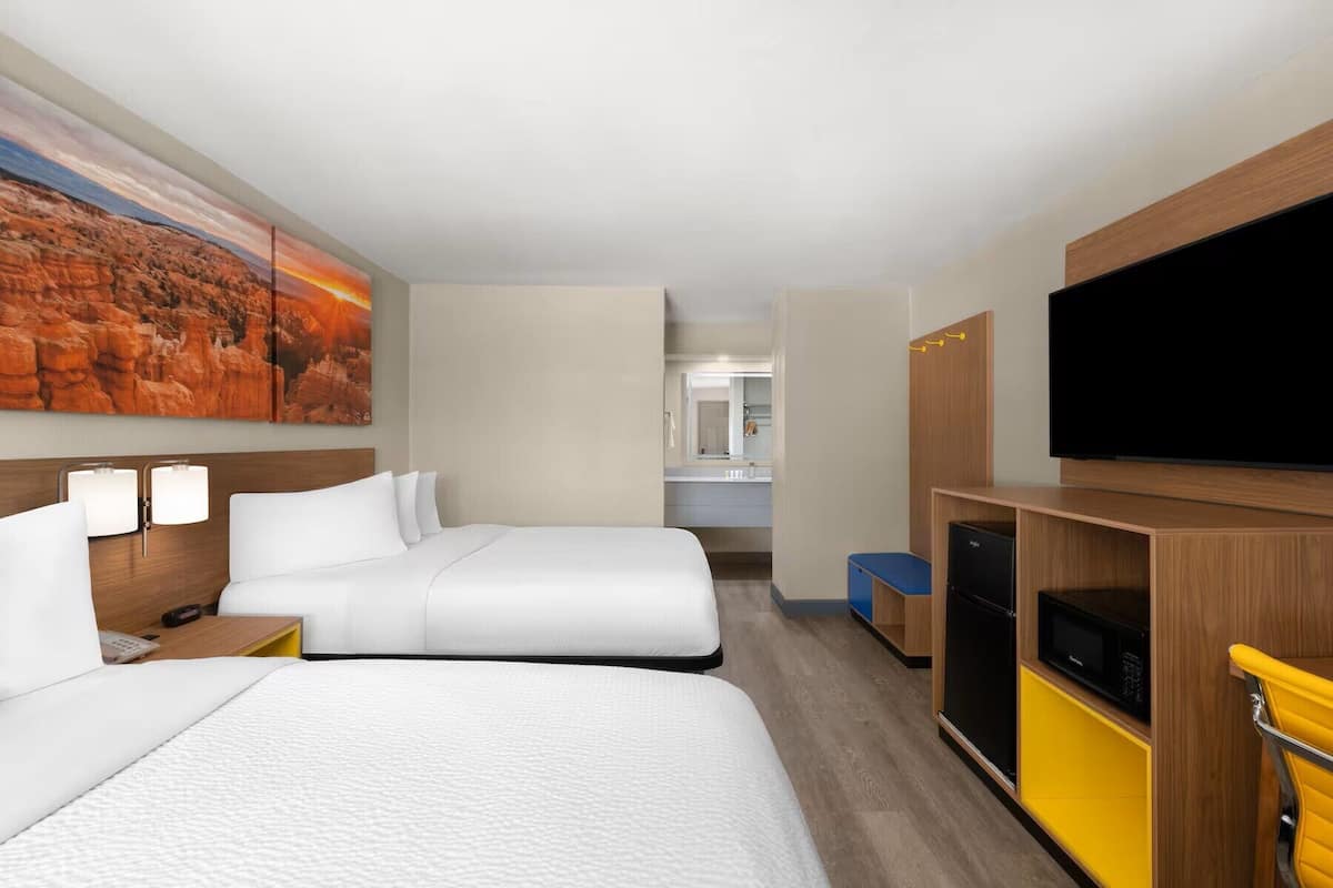 Ein Hotelzimmer mit zwei Betten, einem Fernseher, einer Mikrowelle und einer kleinen Küchenzeile.