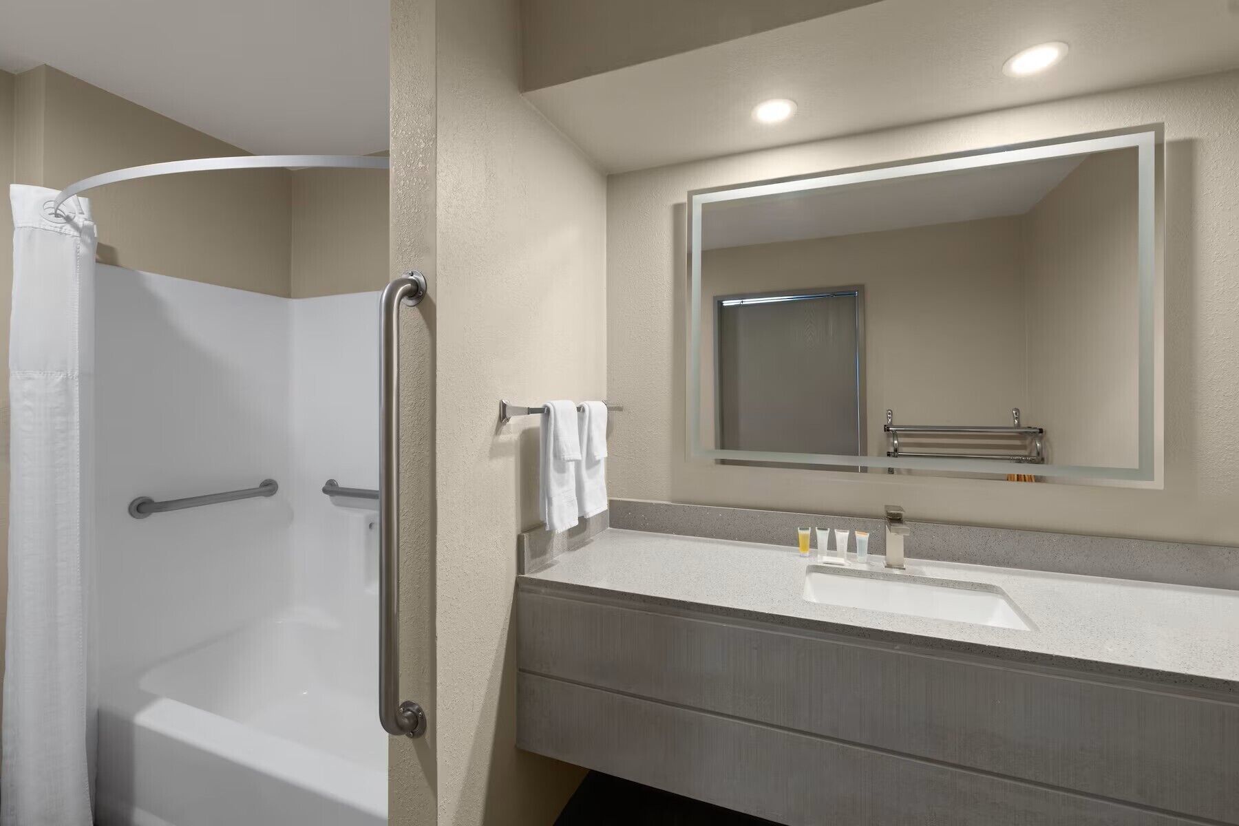 Un baño con bañera, ducha, lavabo con espejo y un perchero para toallas.