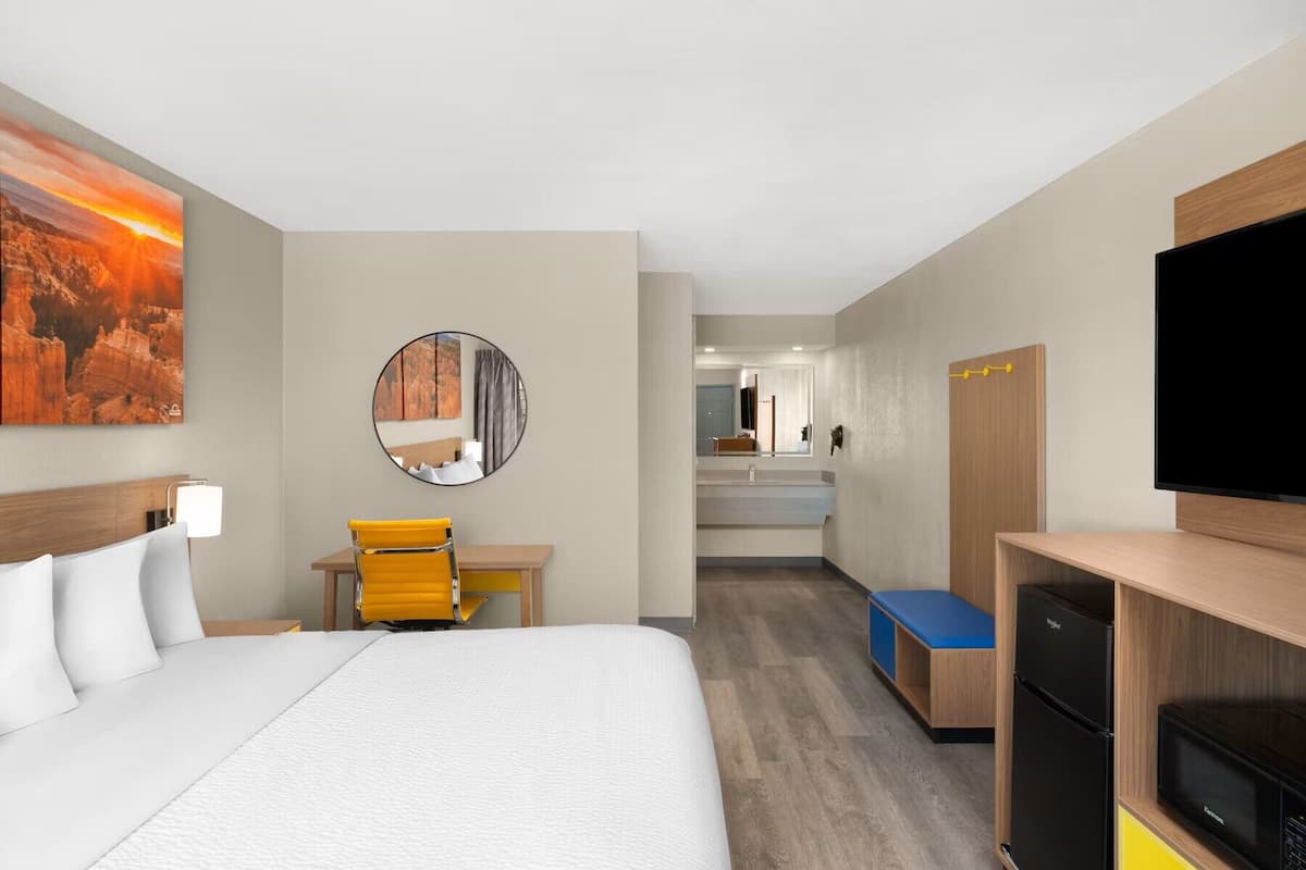 Ein Hotelzimmer mit Bett, Schreibtisch mit Stuhl, Spiegel, Fernseher und einer Küchenzeile.
