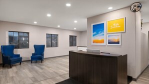 A reception area with a desk, two blue chairs, a wall-mounted mirror, and framed artwork. - Days Inn by Wyndham Safford, AZ (Safford)