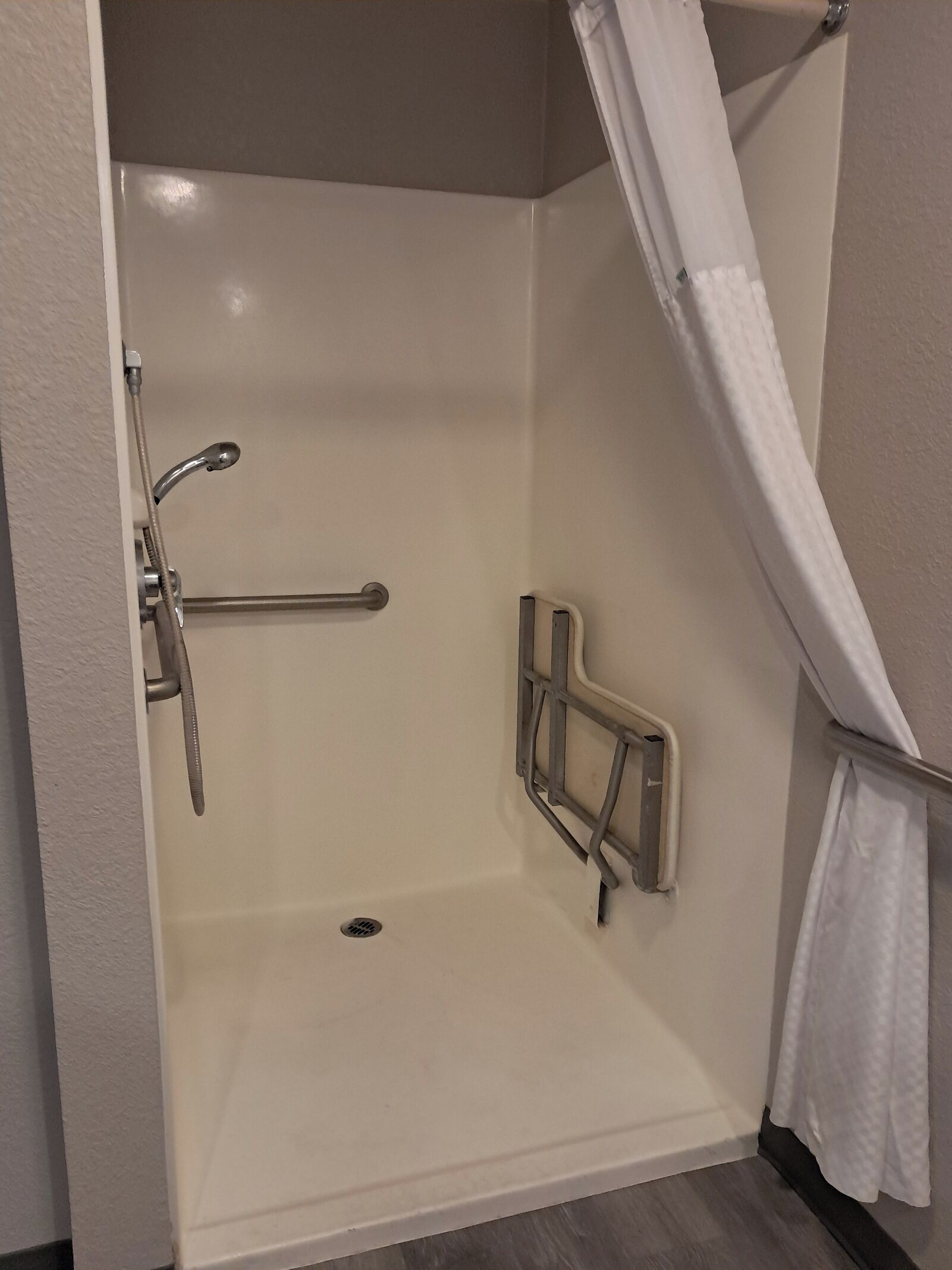 Douche met toegankelijkheid voor rolstoelen, met een handgreep, douchekop en gordijn.