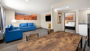 A hotel room with a blue sofa, a wooden dining table, a bed, and a kitchen area. - Days Inn by Wyndham Safford, AZ (Safford)