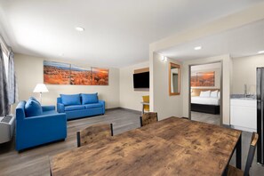 Habitación de hotel con un sofá azul, una mesa de comedor de madera, una cama y una zona de cocina.