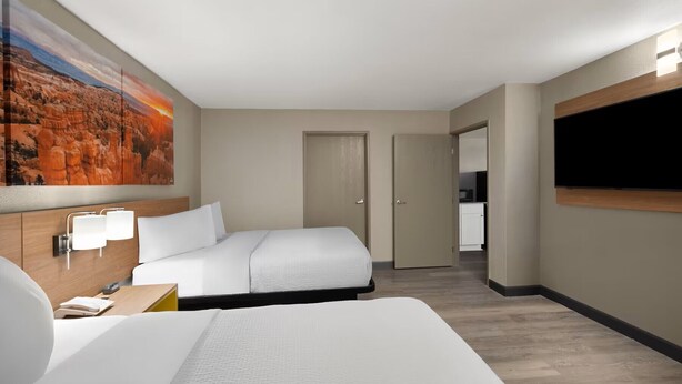 A hotel room with a bed, bedside tables, a painting, a TV, and a door leading to a kitchenette. - Days Inn by Wyndham Safford, AZ (Safford)