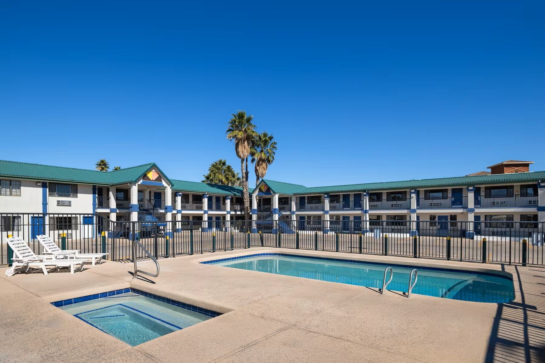 A hotel with a swimming pool, multiple balconies, and a clear blue sky.
