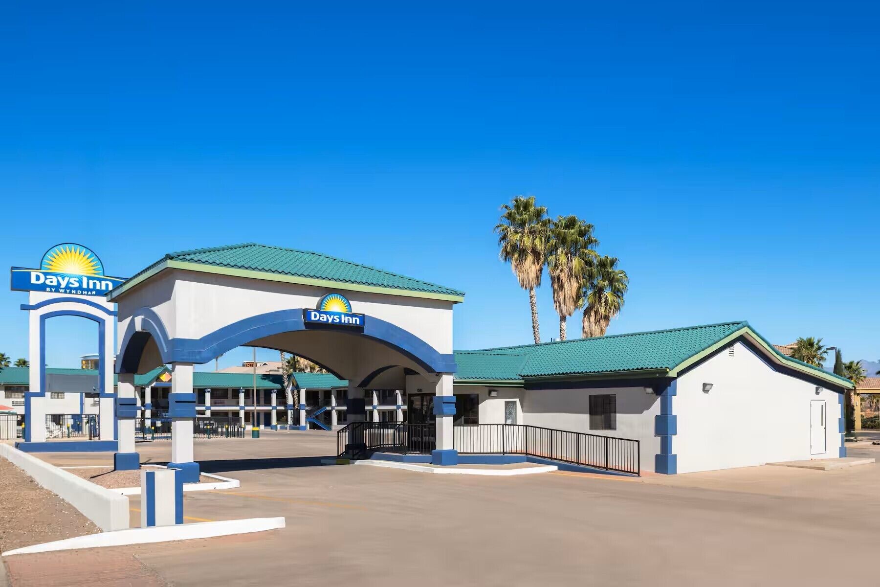 A Days Inn by Wyndham with a clear sky, palm trees, and a simple entrance with a blue and white color scheme.