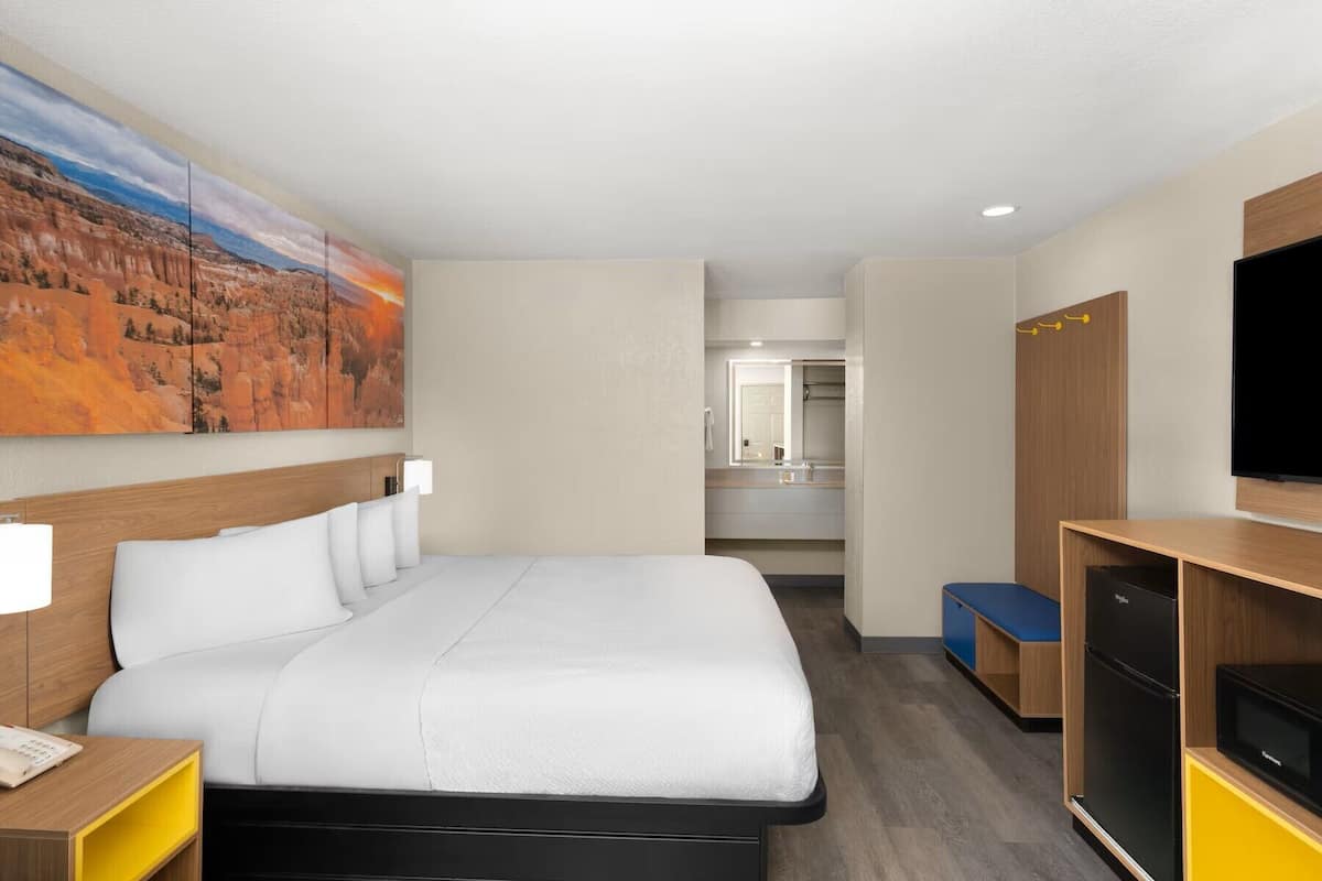 Ein Hotelzimmer mit Bett, Fernseher, Schreibtisch, Spiegel und einem Landschaftsbild.