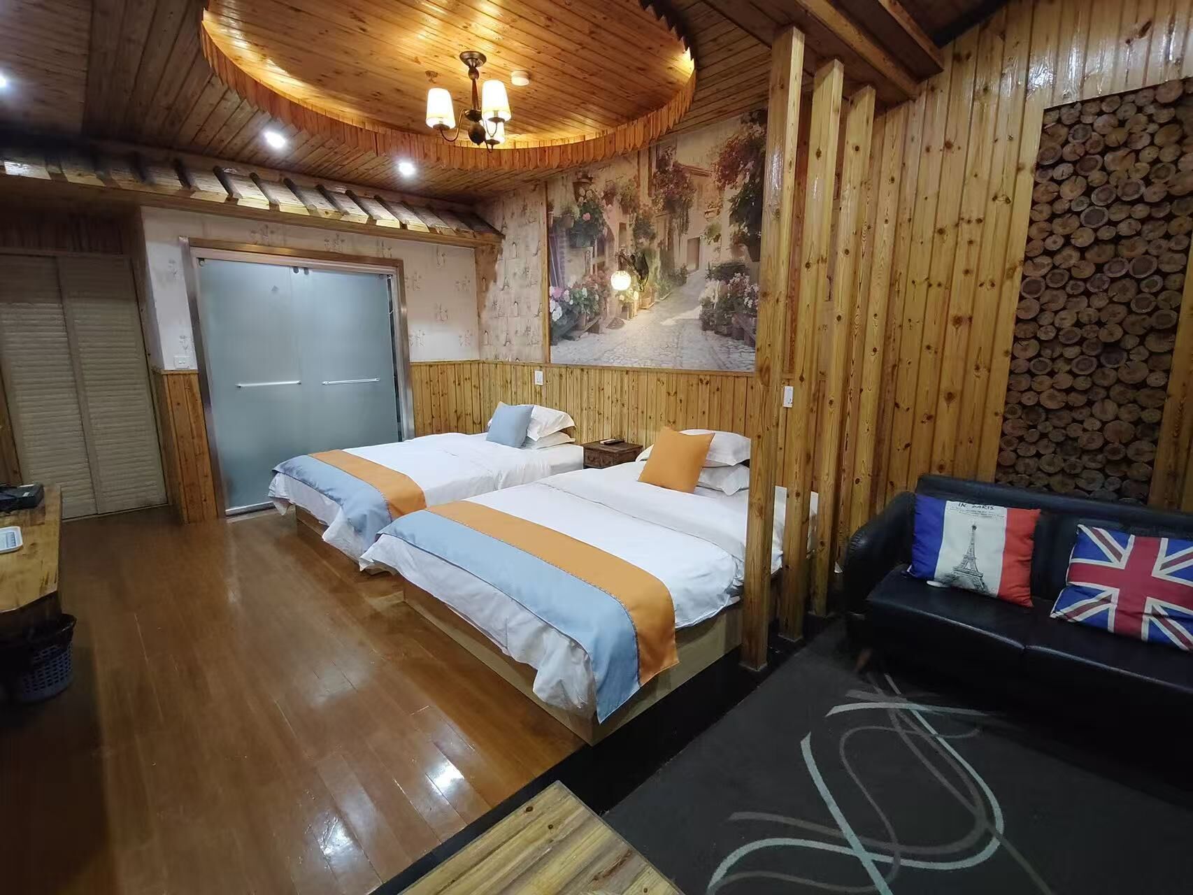 A room with two beds, a wooden ceiling, a wall with a mural, and a sofa with flags.