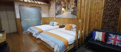 A room with two beds, a wooden ceiling, a wall with a mural, and a sofa with flags.