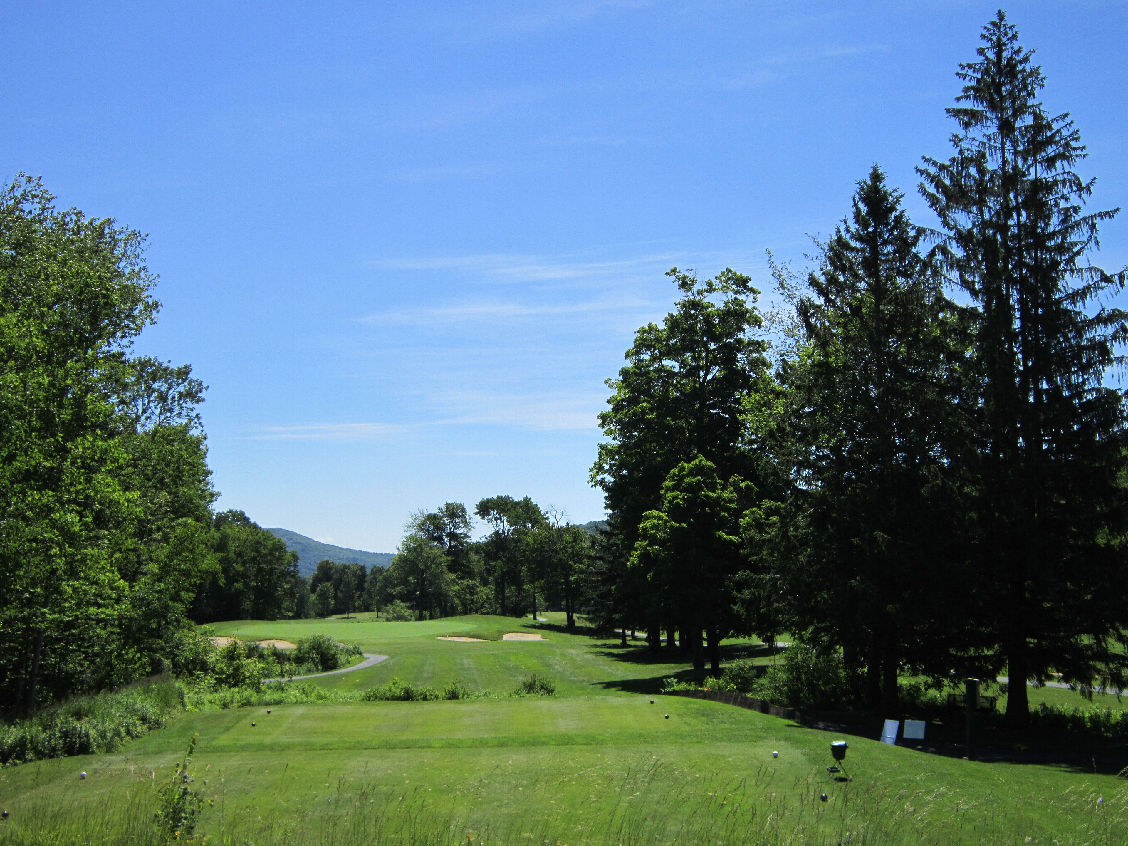 Ein Golfplatz mit blauem Himmel, üppigem Grün und einem entfernten Berg.