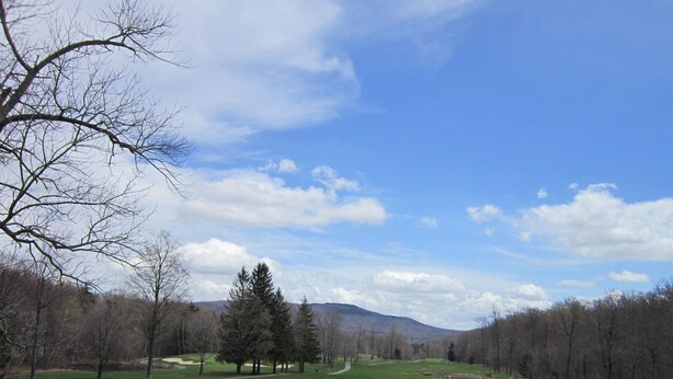 A golf course with sand bunkers, a clear sky, and a mountainous backdrop.