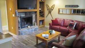 A living room with a stone fireplace, a red leather sofa, a wooden coffee table, and a mounted television.