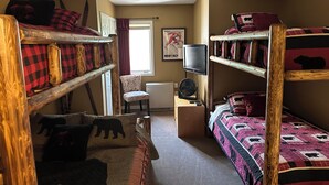 A dormitory room with bunk beds, a chair, a television, and a radiator.